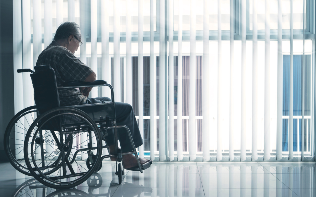 Sad elderly man in a wheelchair at a nursing home looking out the windows