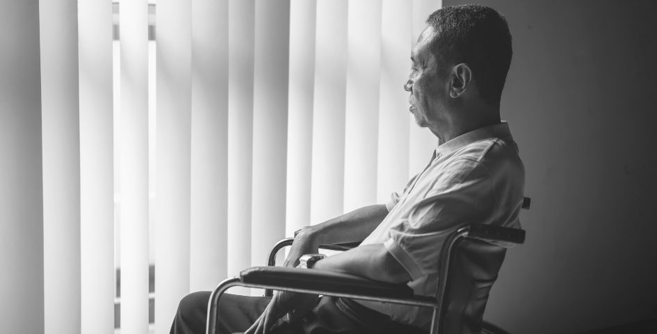 an elderly gentleman in a wheelchair in a nursing home sadly staring out the window