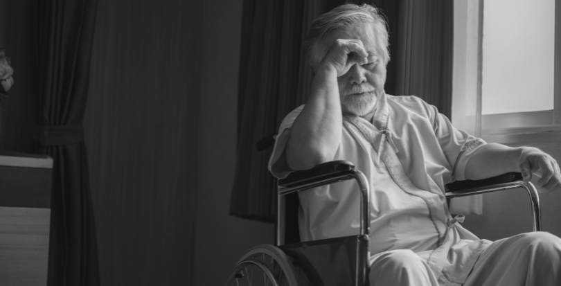 Sad neglected elderly man sitting in nursing home wheelchair looking out window