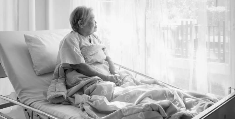 Sad woman in nursing home hospital bed looking out the window